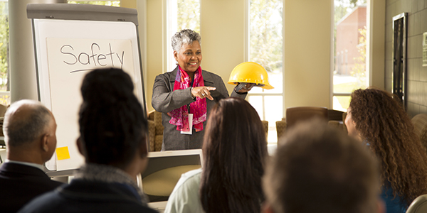 A woman teaching a safety class, holding up a hard hat