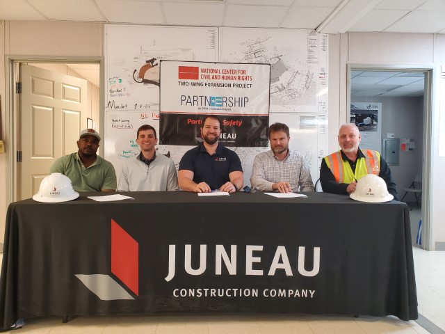 Seated at a table the signatories for Juneau Construction Company and OSHA sign the agreement.