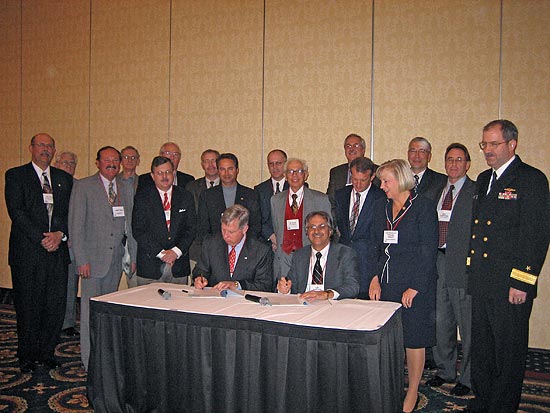 Seated (L to R): Malcolm P. Branch, President, Virginia Ship Repair Association and Leo Edwards, <br /> Acting Area Director, OSHA Norfolk Area Office. Standing to the right of the signing table: U. S. <br /> Congresswoman, Thelma Drake and Rear Admiral John Clarke Orzalli, Commander, Mid-Atlantic Regional <br /> Maintenance Center. Standing behind the signatories are several of the partnership participants.