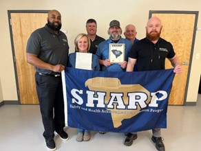 Pictured holding the SHARP flag are Phoenix Specialty Manufacturing safety coordinator along with a staff member, and SC OSHA Consultation supervisor Joe Lam, IH Supervisor Keith Davis, Safety Consultant James Berry and Consultation Program Manager Kenyarda Edwards
