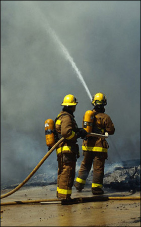 Firemen with hose spraying into smokey background