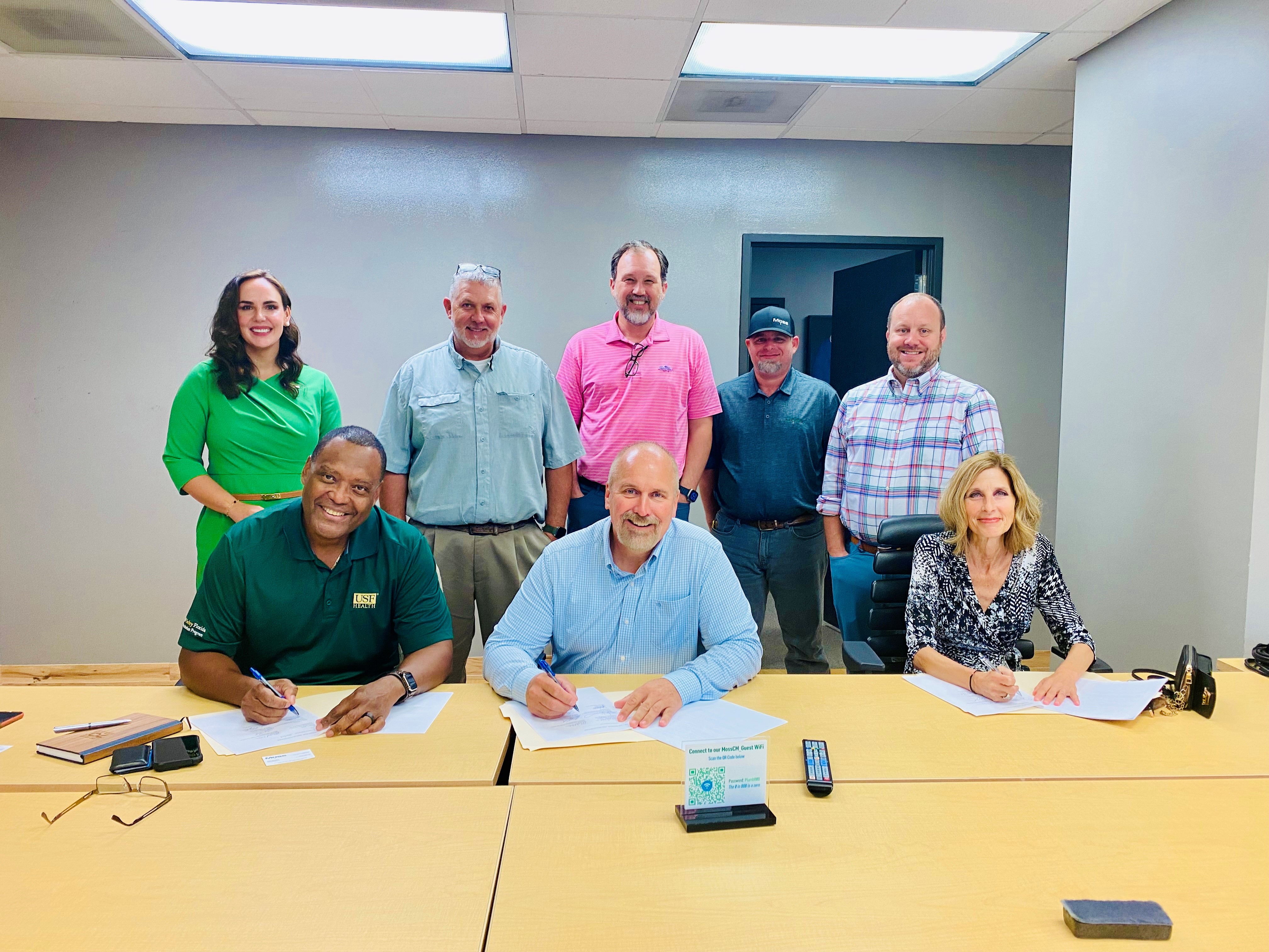 Seated at a table, Brian L. Warrick, Mike Svac and Danelle Jindra sign the agreement. Standing behind them are representatives from Moss & Associates and OSHA.
