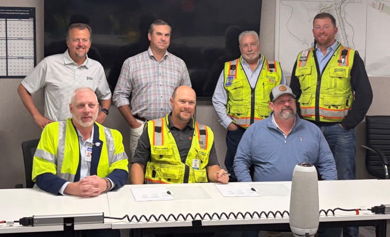 Seated at a table, Jeff Stowowy, Area Director, Atlanta West Area Office, Jason Hodges, Project Director and John Case, Project Safety Director with Brasfield & Gorrie, LLC, signed the Partnership agreement with a small group standing behind them. 