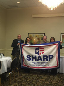 Sam Gualardo presents the SHARP flag to Karina Kolm, Safety Coordinator; Tom Hutchison, Plant Manager; and Patty Sweasy, Safety Manager