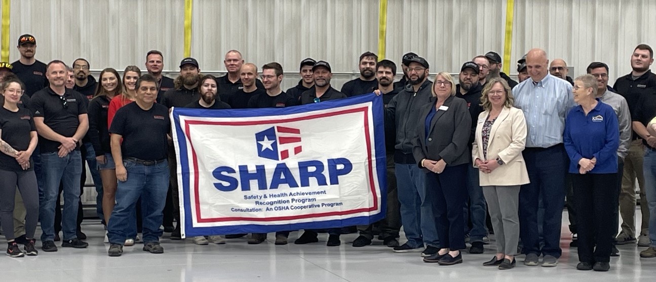 Employees and management stand with the SHARP flag
